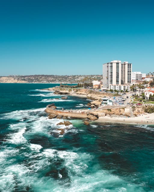 Aerial view of the cliffs, the surf and the ocean at La Jolla Cove, with people walking.