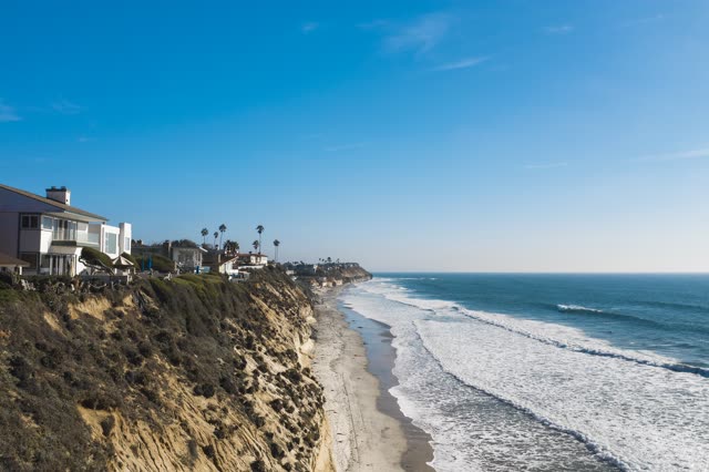 Low aerial view of the cliffs, the surf and palm trees in Encinitas.