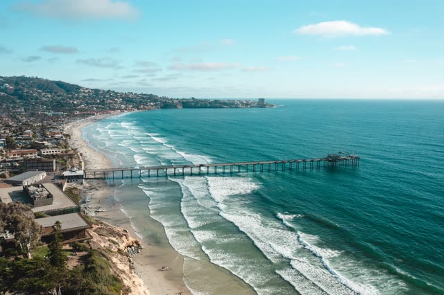 Aerial view of the beach, the surf and the pier at La Jolla Farms, with people walking.