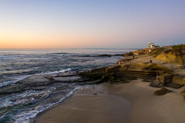 Low aerial view of the cliffs, the surf and the ocean at La Jolla Cove, with people walking.