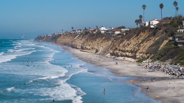 Aerial view of the beach, the surf and palm trees in Encinitas, with people walking.
