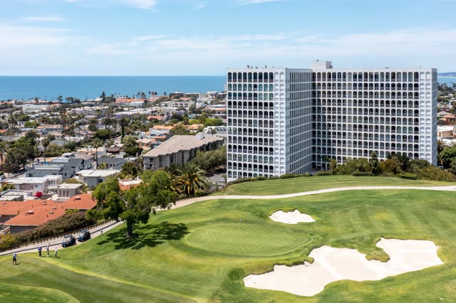 Aerial view of a residential street, palm trees and the ocean at La Jolla Country Club, with people walking.