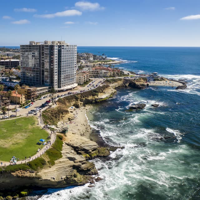 Aerial view of the cliffs, the ocean and homes at La Jolla Cove, with people walking.