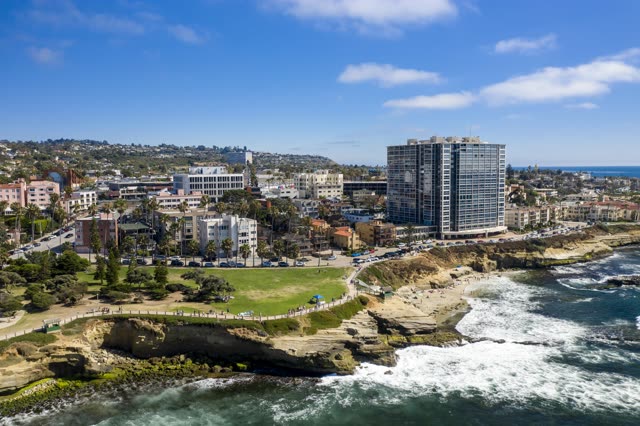 Aerial view of the cliffs, the surf and palm trees at La Jolla Cove, with people walking.