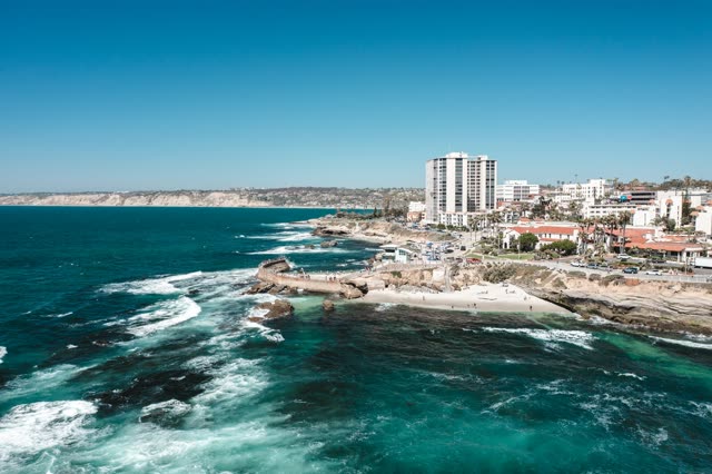Aerial view of the cliffs, the surf and palm trees at La Jolla Cove, with people walking.