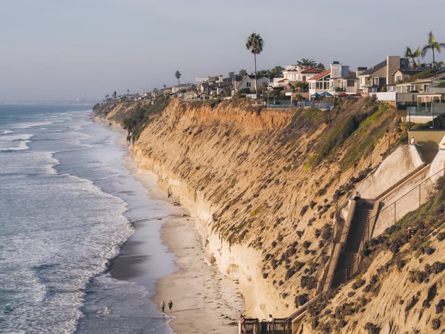 Elevated view of the cliffs, the surf and palm trees in Encinitas, with people walking.