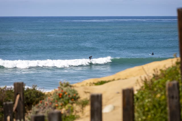 Elevated view of the cliffs, the surf and the ocean in Pacific Beach, with surfers out.