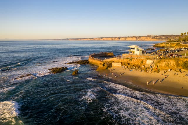 Aerial view of the cliffs, the surf and the ocean at La Jolla Cove, with people walking.