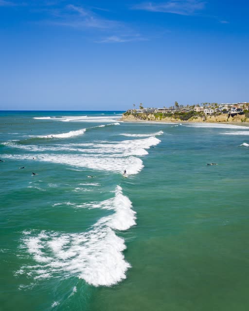 Low aerial view of the beach, the surf and the ocean in Pacific Beach, with surfers out.