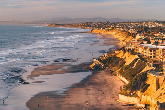 Aerial view of the cliffs, the ocean and homes in Del Mar, with people walking.