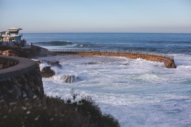 Elevated view of the cliffs, the surf and the ocean at La Jolla Cove, with people walking.