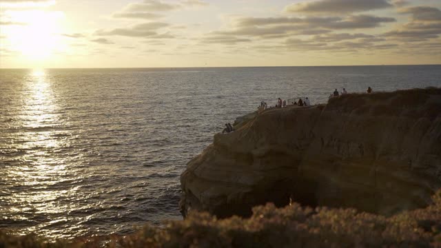 Elevated view of the cliffs, the ocean and open country at Sunset Cliffs, with a crowd gathered.
