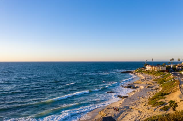 Aerial view of the cliffs, the surf and palm trees at Windansea, with people walking.
