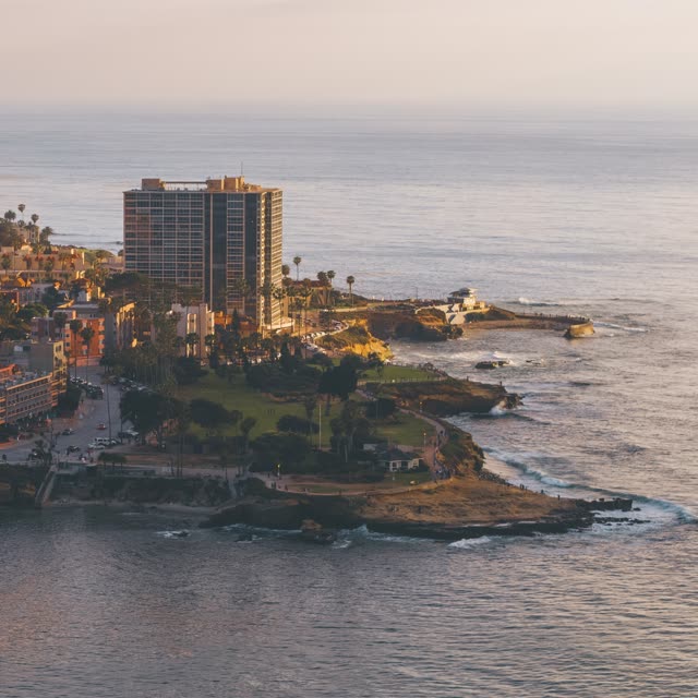 Aerial view of the cliffs, palm trees and the ocean at La Jolla Cove, with people walking.
