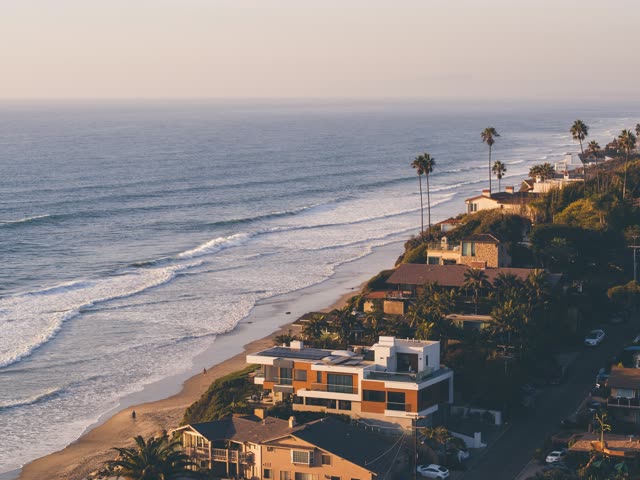 Aerial view of the beach, the surf and palm trees at Moonlight Beach, with people walking.