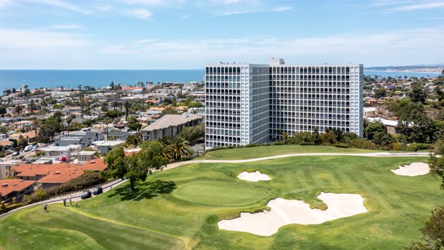 Aerial view of a residential street, palm trees and the ocean at La Jolla Country Club, with people walking.