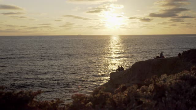 Elevated view of the cliffs, boats and the ocean at Sunset Cliffs, with a crowd gathered.