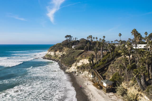 Aerial view of the cliffs, the surf and palm trees at Swamis, with people walking.