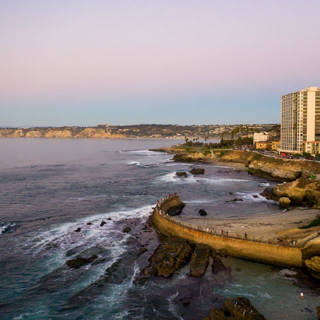 Aerial view of the cliffs, the surf and the ocean at La Jolla Cove, with people walking.