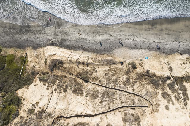 Aerial view of the cliffs, the surf and the ocean in Encinitas, with people walking.