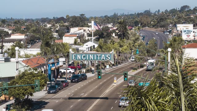 Low aerial view of the downtown streets, palm trees and homes at Downtown Encinitas, with people walking.