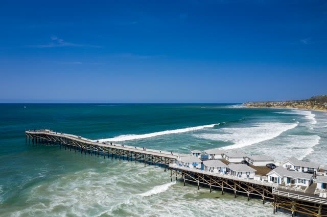 Aerial view of the beach, the surf and the pier in Pacific Beach, with people walking.