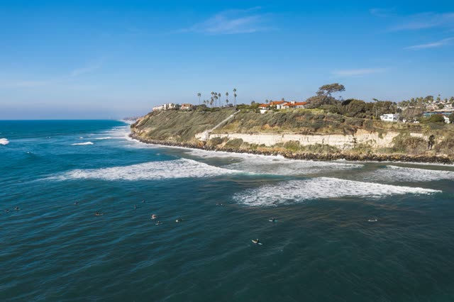 Aerial view of the cliffs, the surf and palm trees at Swamis, with surfers out.