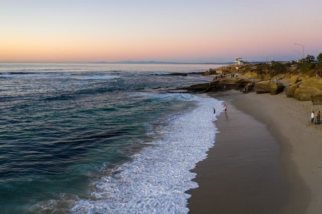 Low aerial view of the beach, the surf and the ocean at La Jolla Cove, with people walking.