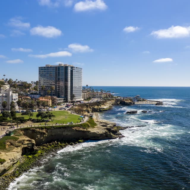 Aerial view of the cliffs, the surf and palm trees at La Jolla Cove, with people walking.