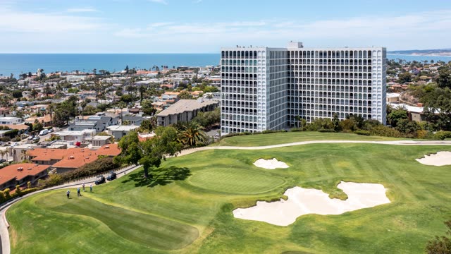 Aerial view of a residential street, palm trees and the ocean at La Jolla Country Club, with people walking.