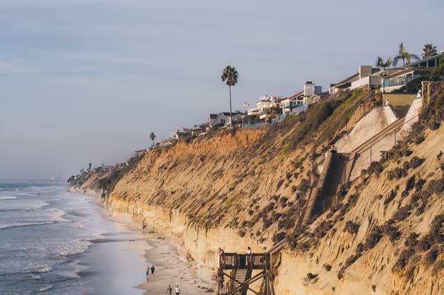 Elevated view of the cliffs, the surf and palm trees in Encinitas, with people walking.