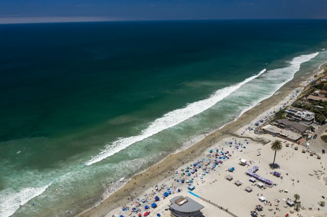 Aerial view of the beach, the surf and palm trees at Moonlight Beach, with a crowd gathered.