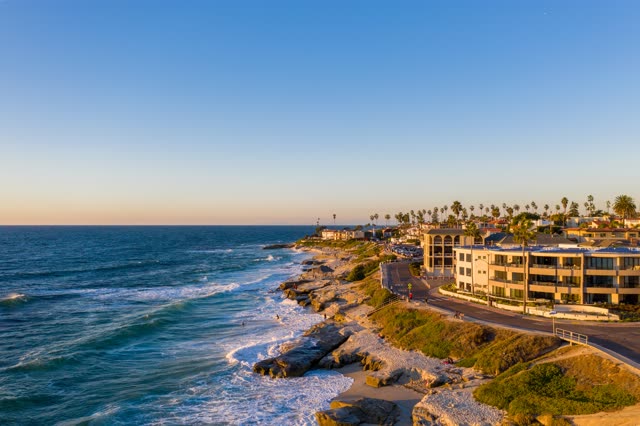 Aerial view of the cliffs, the surf and palm trees at Windansea, with people walking.