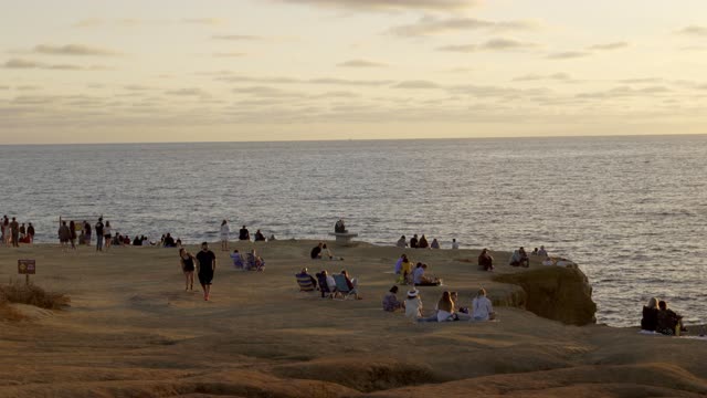 Elevated view of the cliffs, the ocean and open country at Sunset Cliffs, with a crowd gathered.