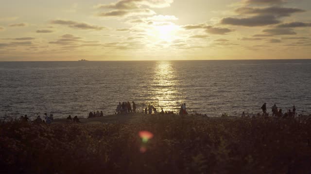 Elevated view of the cliffs, boats and the ocean at Sunset Cliffs, with a crowd gathered.