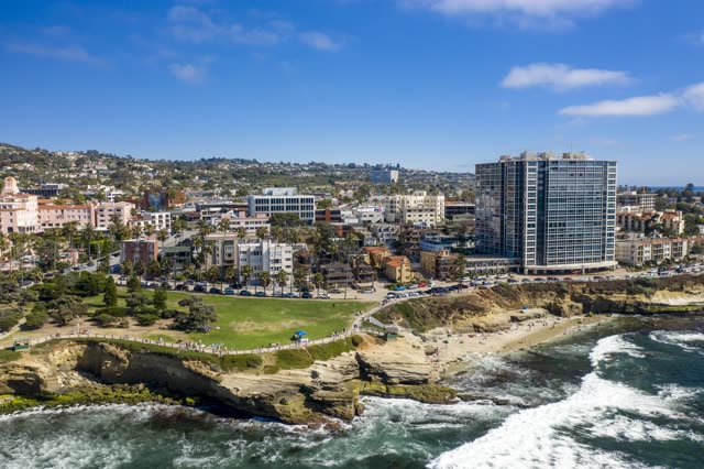 Aerial view of the cliffs, the surf and palm trees at La Jolla Cove, with people walking.