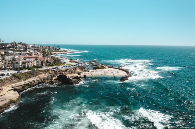 Aerial view of the cliffs, the surf and the ocean at La Jolla Cove, with people walking.