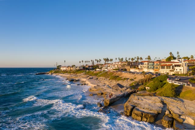 Elevated view of the cliffs, the surf and palm trees at Windansea, with people walking.