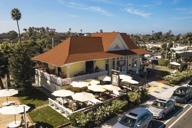 Low aerial view of the downtown streets, palm trees and homes in Encinitas, with people eating outside.