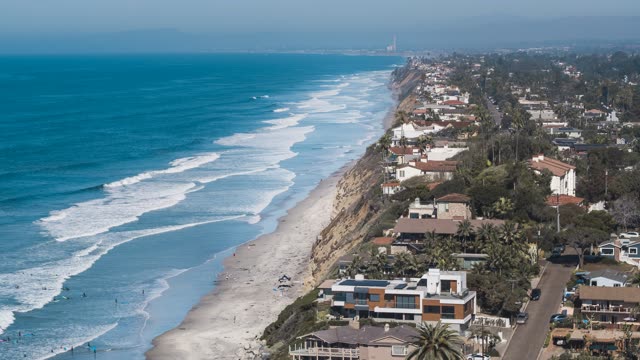 Aerial view of the beach, the surf and palm trees at Moonlight Beach, with people walking.